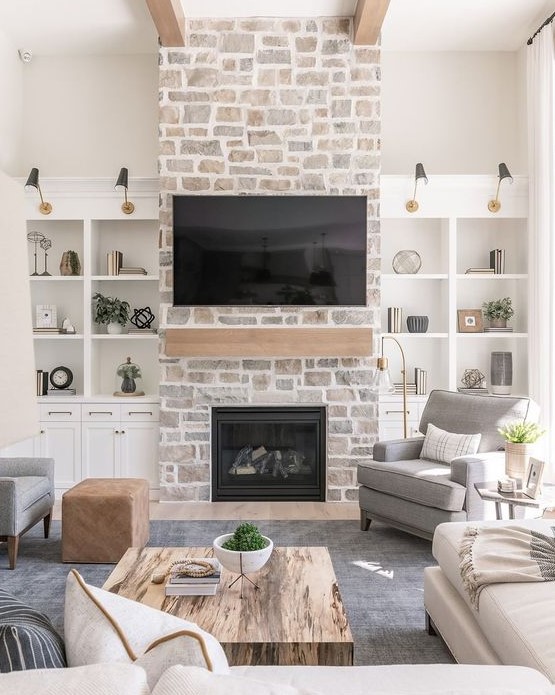 a whitewashed stone fireplace with a wooden mantel and storage units on each side of it is a cozy and chic touch to the room decor