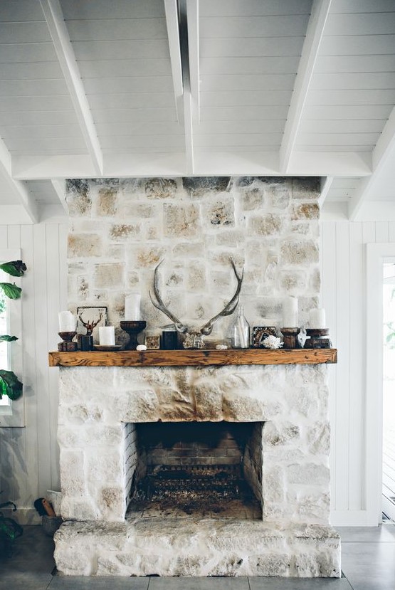 a whitewashed stone fireplace with a wooden mantel with candles, antlers and more rustic decor for a cozy feel