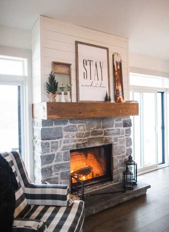 a whitewashed stone fireplace with lanterns by its side, a wooden mantel with artworks and potted plants