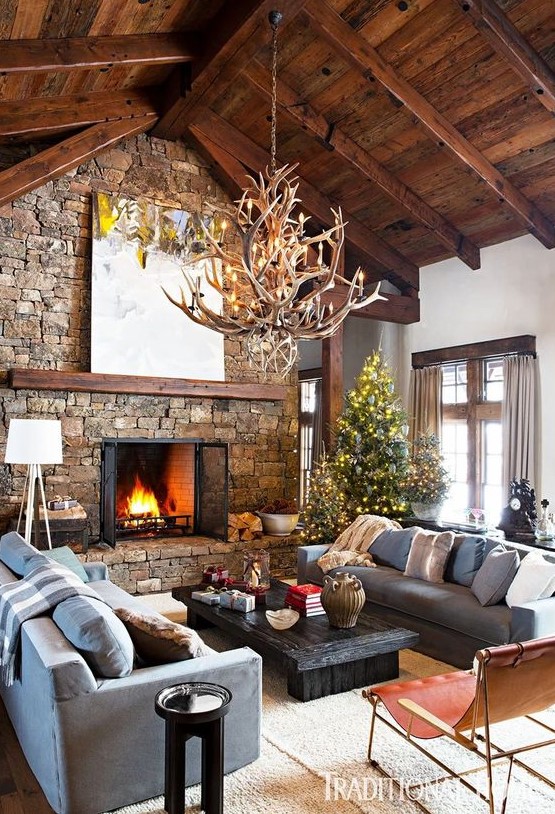 an inviting chalet living room with a wooden ceiling with beams, a stone fireplace, an antler chandelier and chic and cool furniture