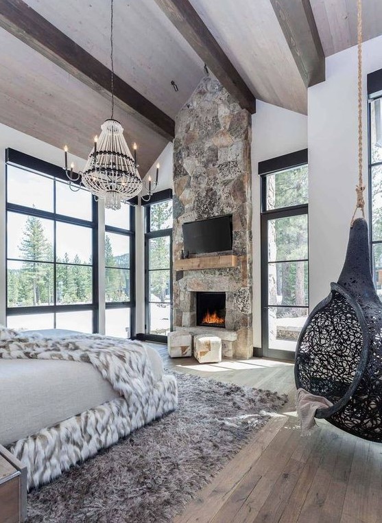 an ultra-modern chalet bedroom with a stone fireplace, a suspended chair, a catchy chandelier and lots of faux fur