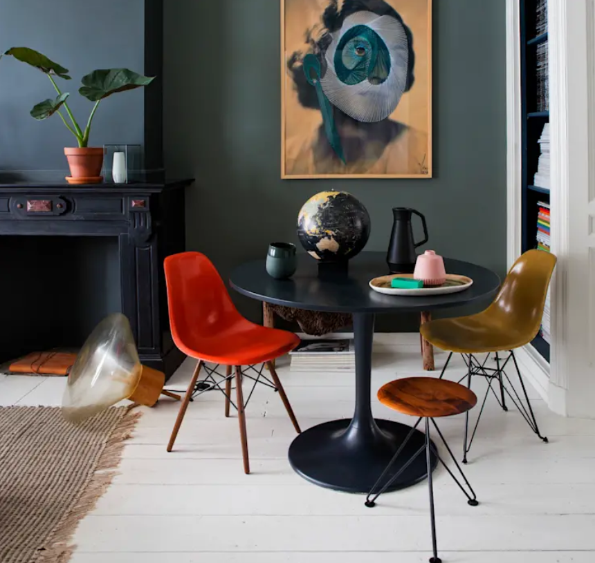 The bold dining nook is done with colorful mismatching chairs and a black shiny round table, it's next to the fireplace