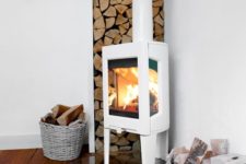02 a modern white wood burning stove on a glass stand, with firewood in the corner and baskets for firewood