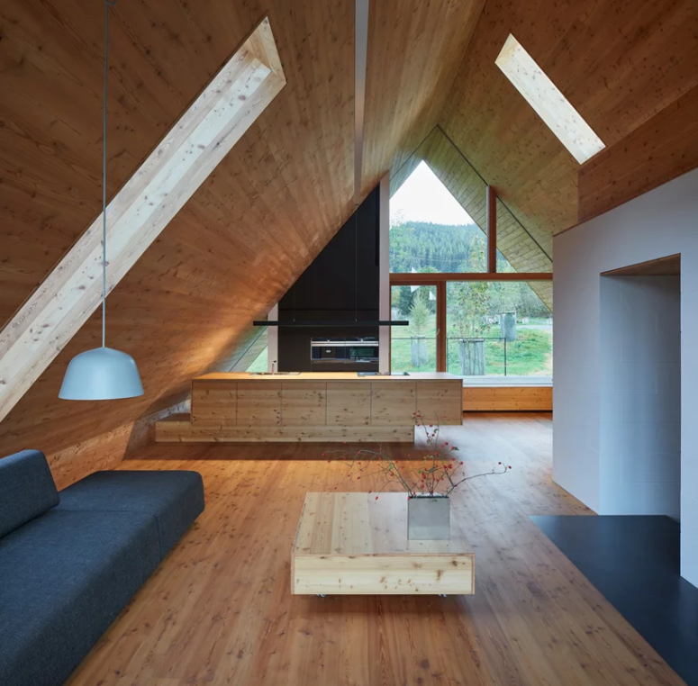 a minimalist open layout living space design Inside there's an open layout with a kitchen and a living space with a glazed wall and skylights