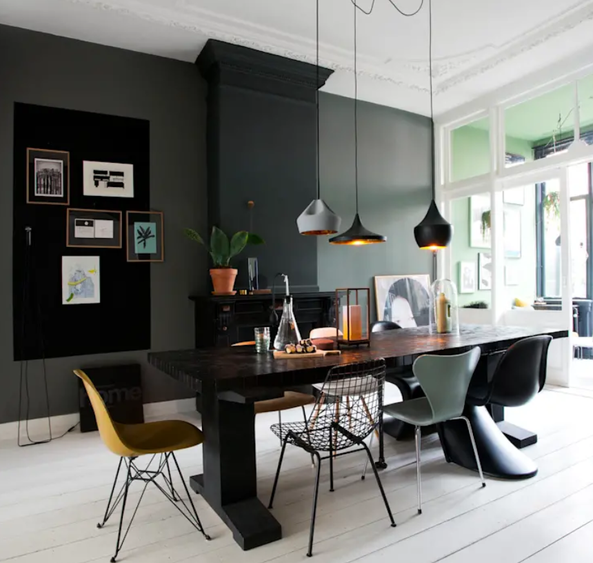 A large dining space is done with a black fireplace, a gallery wall, mismatching chairs, a black wooden table and pendant lamps