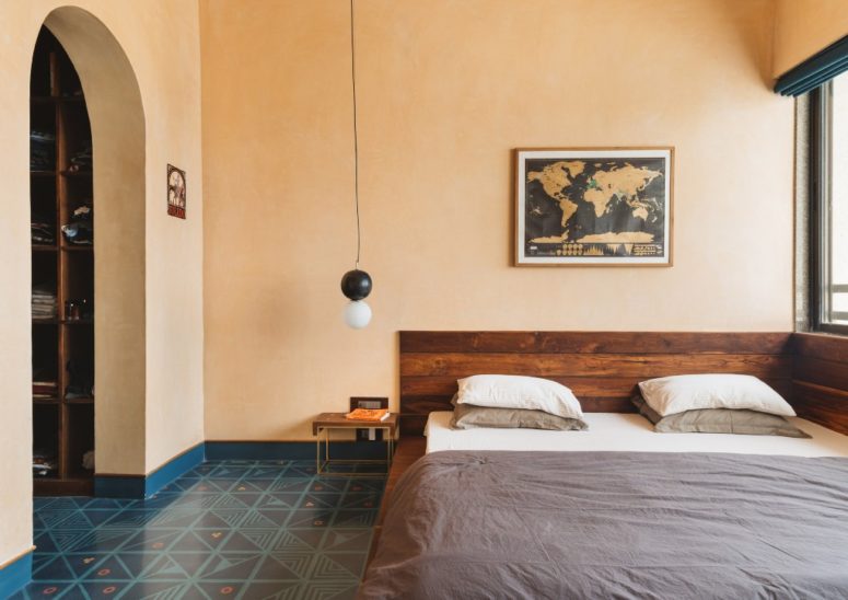 The bedroom is warmer, there's a rich stained wooden bed, a tile floor and lamps