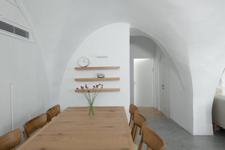 The dining space is done with light-colored wooden dining set and floating shelves