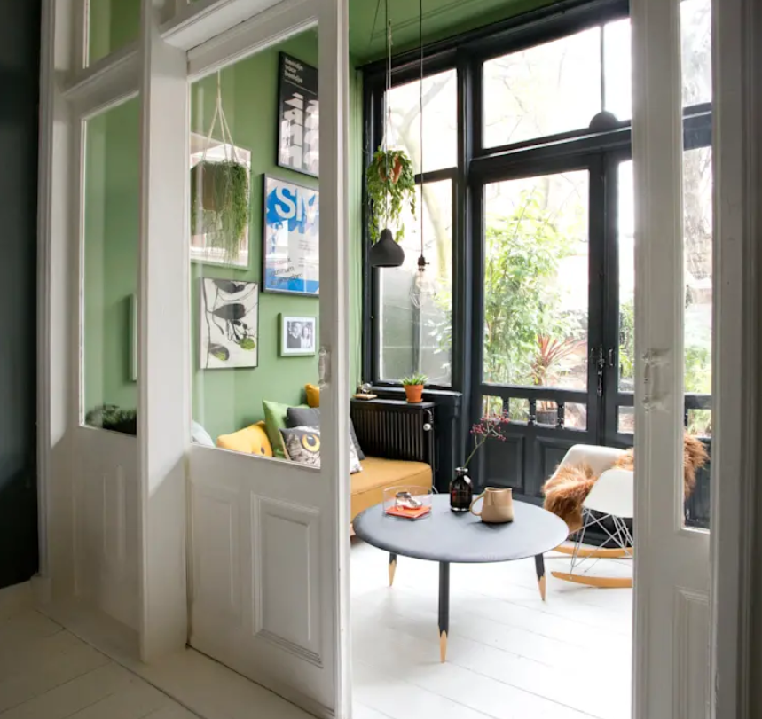There's a sunroom with bright green walls, a glazed wall, pendant lamps and plants and some cool furniture