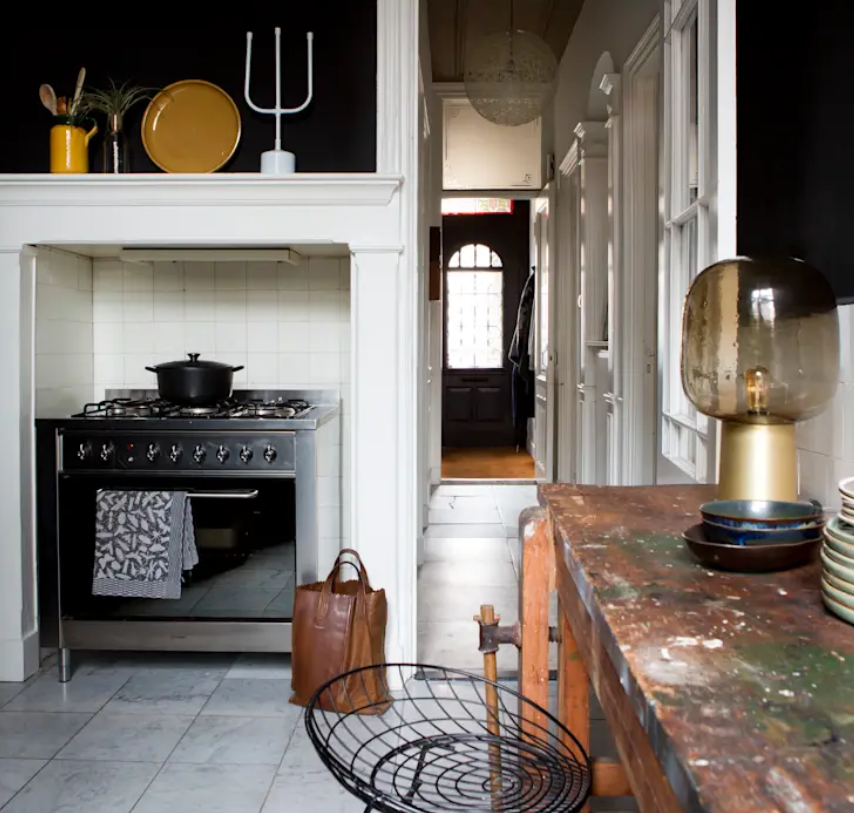The kitchen features a modern cooker, black walls and white tiles, a shabby chic table and some quirky art and lamps