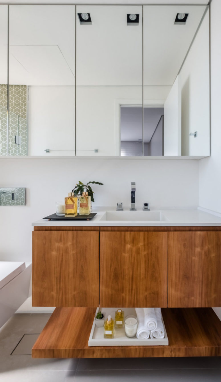 The bathroom is done with grey tiles, a rich-colored vanity is topped with a white countertop