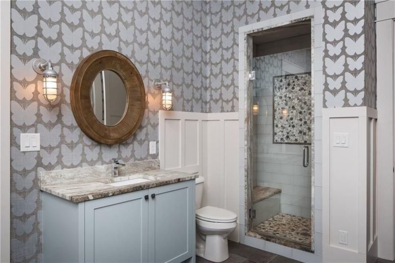 This bathroom is done with butterfly wallpaper, a wood frame mirror and a vanity with a stone countertop
