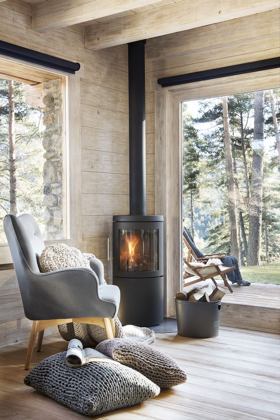 a contemporary cabin space with large windows, wood clad space and a modern wood burning stove in the corner