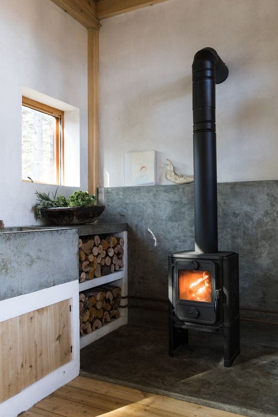 a contemporary kitchen with much concrete in decor and a vintage wood burning stove plus firewood storage