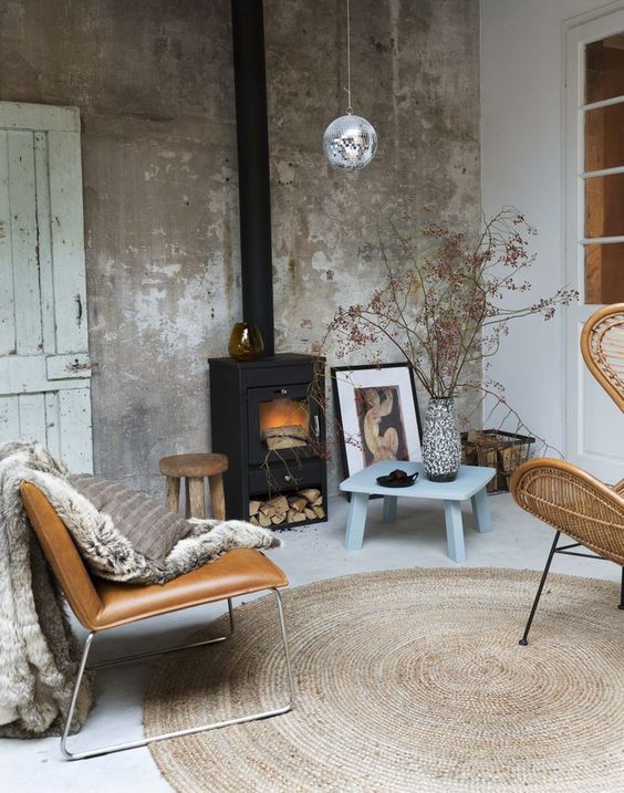 an industrial meets modern space with a black stove, a rough concrete wall and leather and wooden furniture