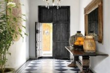 a Spanish entryway with black and white printed tiles, a reclaimed dakr wood door, a heavy console and potted greenery