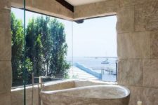 a catchy bathroom with a sea view, stone walls, stone tiles on the floor and a catchy stone bathtub