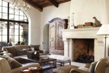 a chic Spanish living room with white plaster walls, reclaimed wood ceiling with beams, neutral furniture and vintage chandeliers