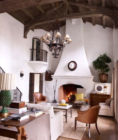 a chic yet small Spanish living room with white plaster walls, a large fireplace, some colored accents and leather chairs