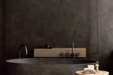 a dark and moody bathroom with a black stone bathtub, a mini side table and a wooden shelf on the wall