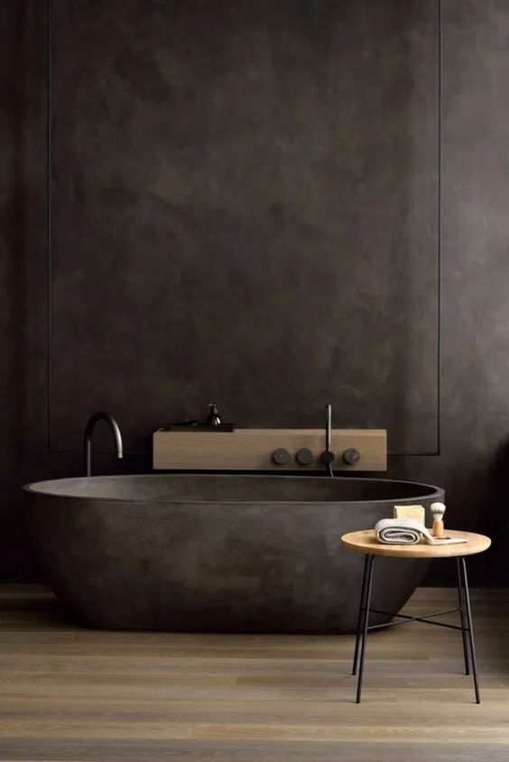 a dark and moody bathroom with a black stone bathtub, a mini side table and a wooden shelf on the wall