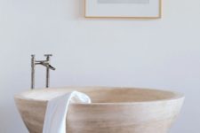 a neutral contemporary bathroom with a bowl-like stone bathtub and a catchy artwork for a modern feel