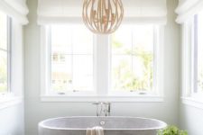 a neutral farmhouse bathroom with printed tiles, a neutral stone bathtub and a round chandelier looks serene