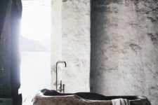 a rough bathroom with a carved stone bathtub that stands out and makes a fashion statement together with a sea view