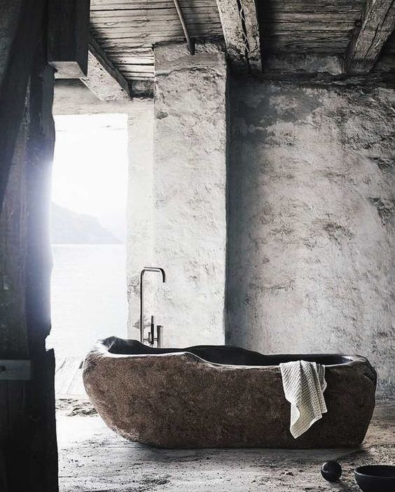 a rough bathroom with a carved stone bathtub that stands out and makes a fashion statement together with a sea view