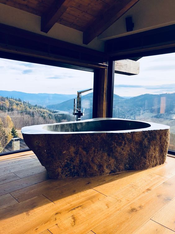 a rustic bathroom with a fantastic view, wooden floors and a dark stone bathtub carved of a single piece of stone