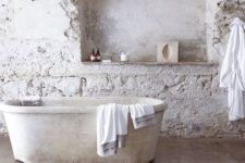 a white bathroom with rough stone tiles, a white stone bathtub and a jute rug is all-natural and relaxing