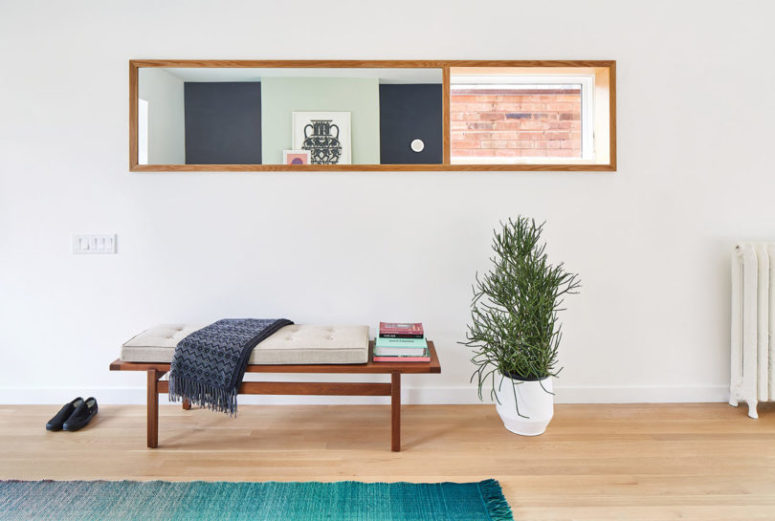 The entryway is clean and simple, with an upholstered bench and a potted plant in a geometric planter The entryway is clean and simple, with an upholstered bench and a potted plant in a geometric planter