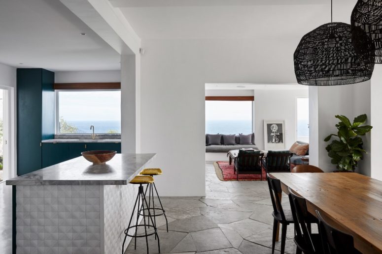 The living room, dining space and kitchen are united in one layout, the kitchen is blue, the dining chairs and chandelier are black