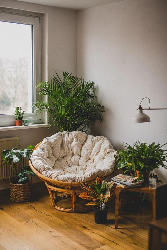 a cozy reading nook with a papasan chair with a neutral futon and lots of potted greenery
