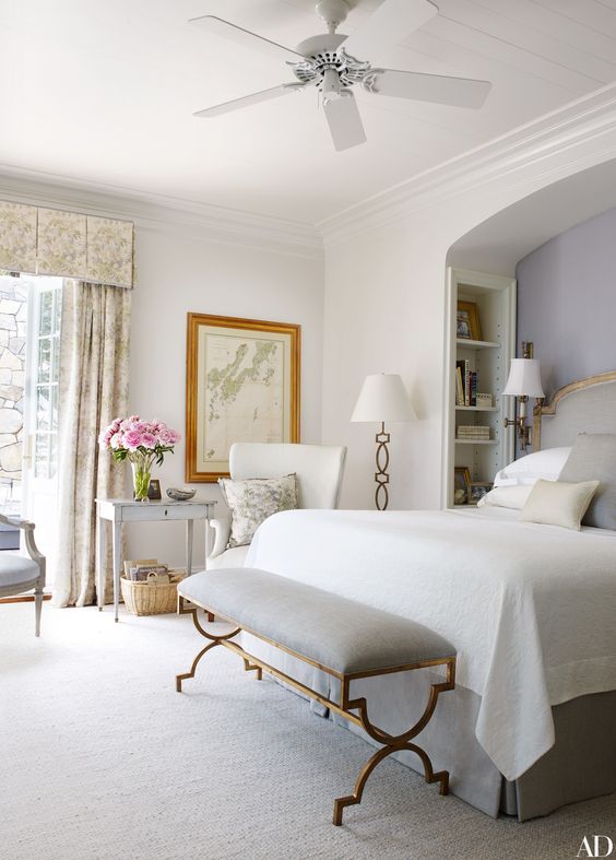 a vintage bedroom done in all neutrals, with a chic bench on brass legs and a matching floor lamp in the corner