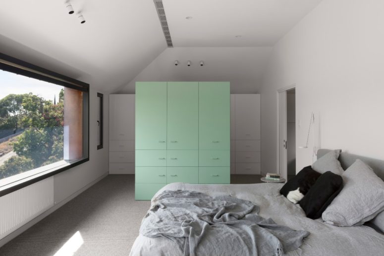 The bedroom features white and mint cabinets, a comfy bed and a view through a large window