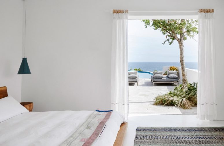 The bedroom is white, there's simple yet chic woodne furniture, blue lamps and an entrance to the terrace