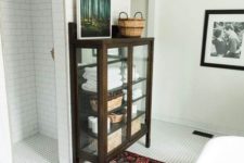 06 a modern bathroom with a bright rug, white tiles all over and a vintage dark stained glass armoire