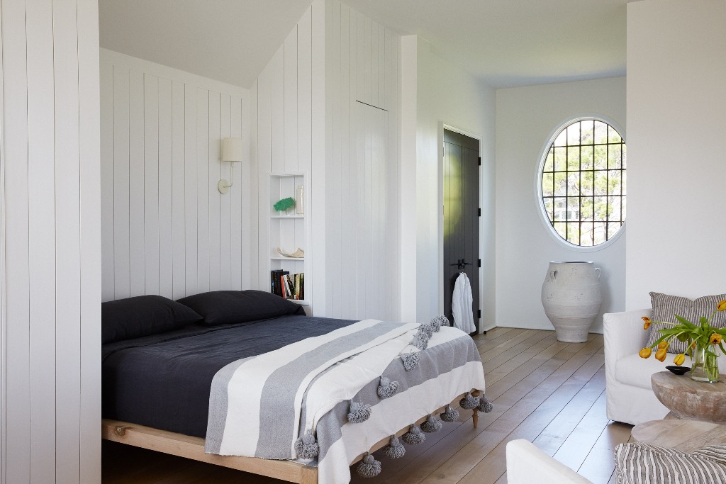 The bedroom is done with white walls, a bed in a niche and a creative round window