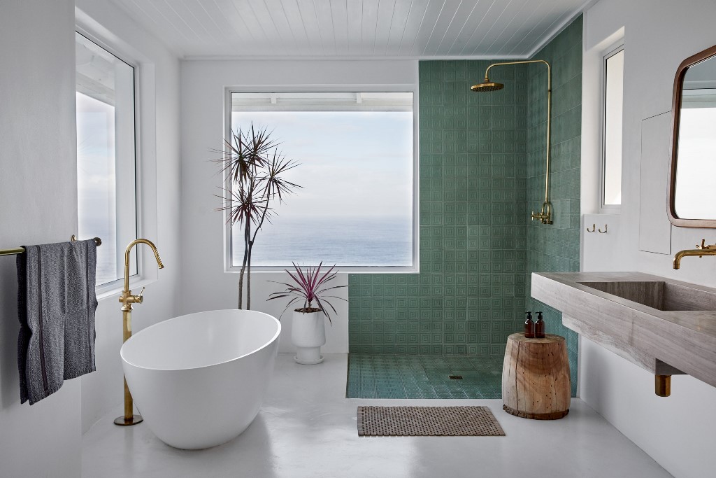 The master bathroom is done with an oval tub, a green tile shower space and a concrete sink