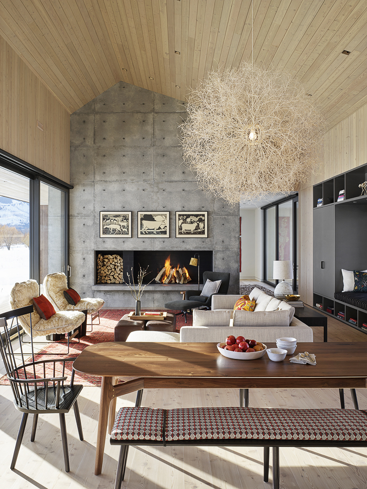 The living room is quirky, with a concrete wall with a fireplace, a catchy chandelier, trendy furniture and a dining space right here