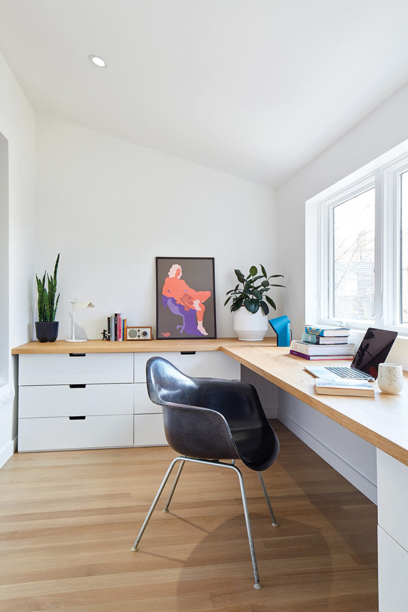 The work space is done with a large corner desk, white cabinets, bold artworks and potted plants