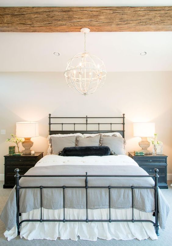 a farmhouse bedroom with a wooden beam on the ceiling and a statement sphere chandelier hanging on it