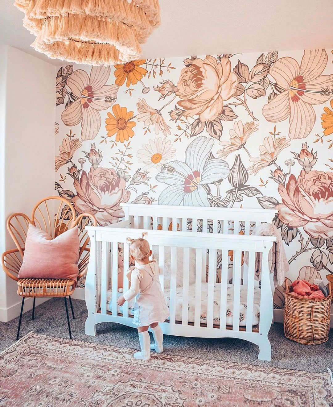 a colorful girl's nursery in peachy and coral with a statement large scale floral print wall that creates a mood here