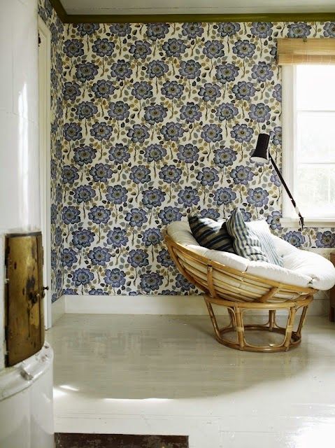 a chic reading nook with a blue wallpaper wall, a rattan papasan chair and graphic pillows