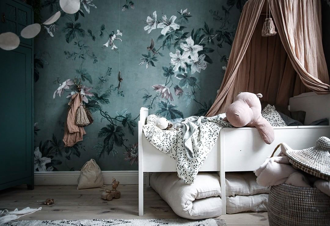 a refined nursery with a green floral accent wall and touches of dark green and soft blush and pink for a chic look