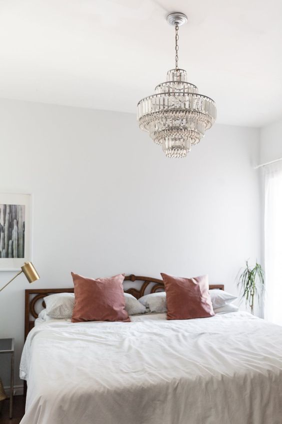 a modern boho bedroom in neutrals and pastels with a statement vintage crystal chandelier over the bed