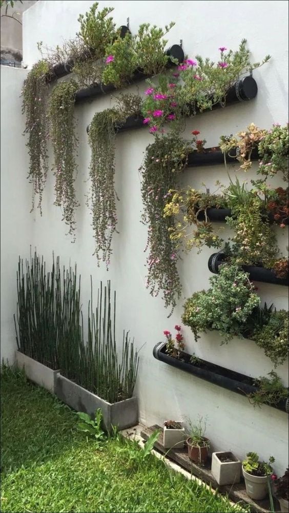 a wall with black metal planters with greenery and bright blooms and concrete planters with grasses