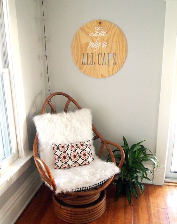 a boho nook with a wooden papasan swivel rocker with faux fur and a bright pillow