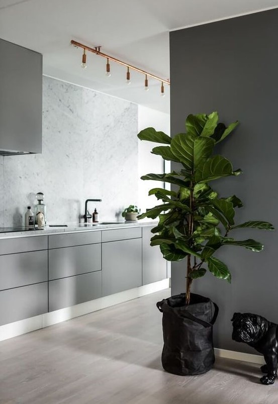 a Nordic kitchen with plain grey cabinets, white countertops and a backsplash, copper bulbs and a grey hood