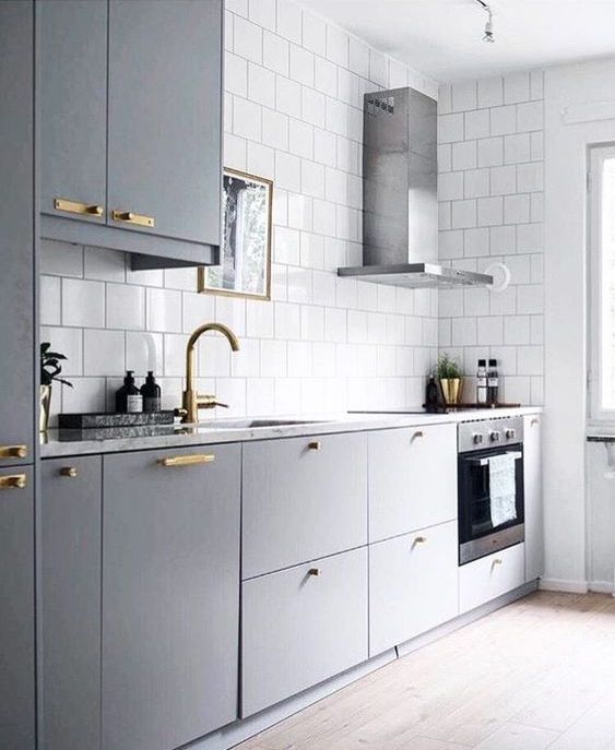 a Scandinavian kitchen with grey cabinets and white square tiles on the walls, a metal hood and gold handles